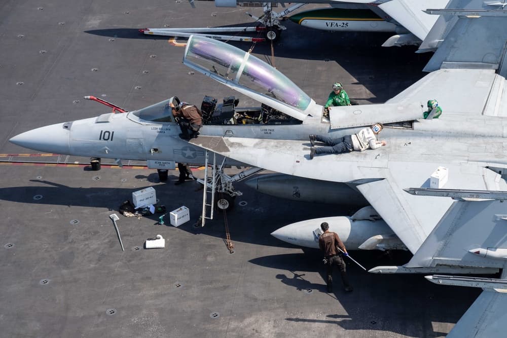 Flight deck crew work alongside an aircraft on a carrier.